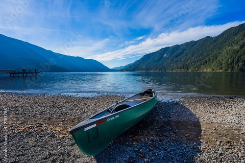 Green canoe left on a rocky beach with a glacier lake and mountains in the background at Lake Crescent, Washington in Olympic National Park
 photo