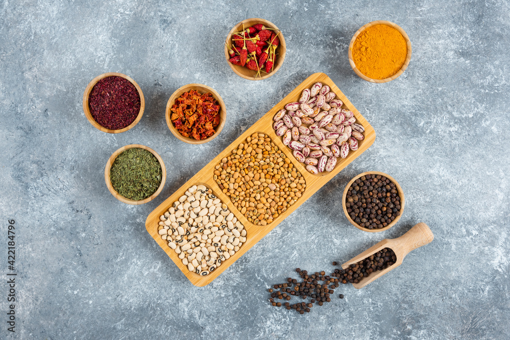 Plates of raw beans and spices on marble background
