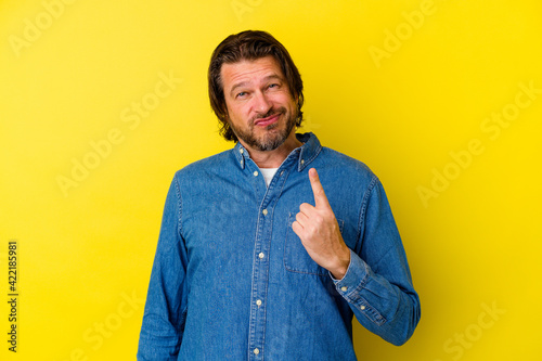 Middle age caucasian man isolated on yellow background pointing with finger at you as if inviting come closer.