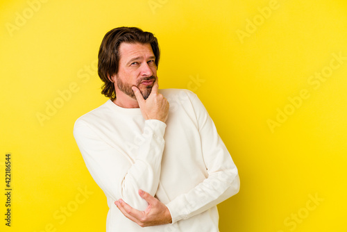 Middle age caucasian man isolated on yellow background suspicious, uncertain, examining you.