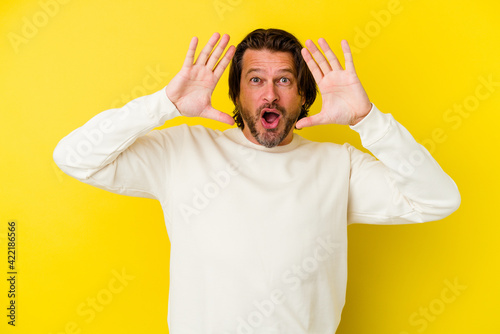 Middle age caucasian man isolated on yellow background celebrating a victory or success, he is surprised and shocked.