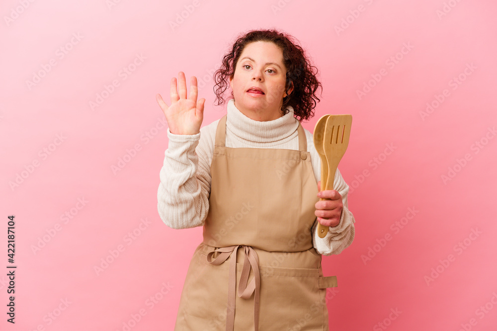 Woman with Down syndrome cooking at home isolated on pink background smiling cheerful showing number five with fingers. Woman with Down syndrome cooking at home isolated on pink background smiling cheerful showing number five with fingers.