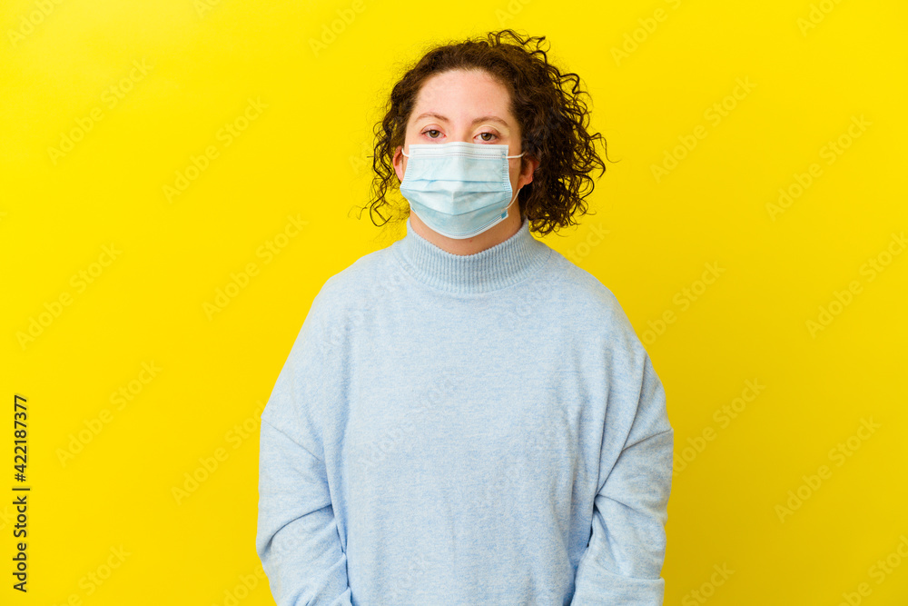 Young woman with Down syndrome wearing an antivirus mask isolated shrugs shoulders and open eyes confused.