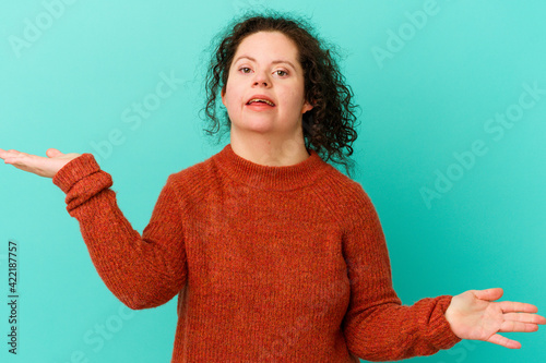 Woman with Down syndrome isolated confused and doubtful shrugging shoulders to hold a copy space.