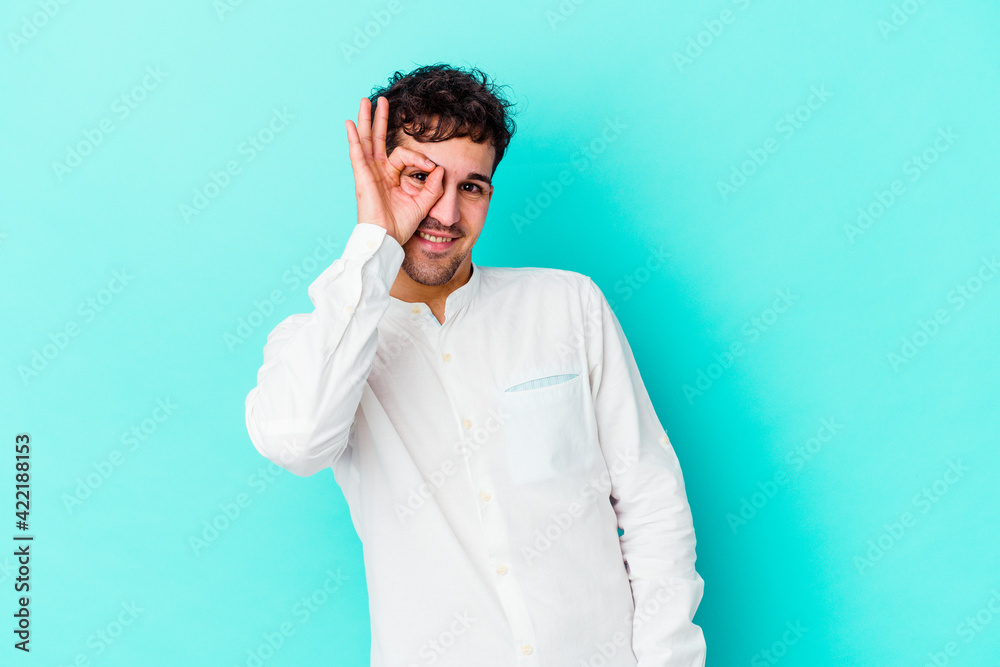 Young caucasian man isolated on blue background excited keeping ok gesture on eye.