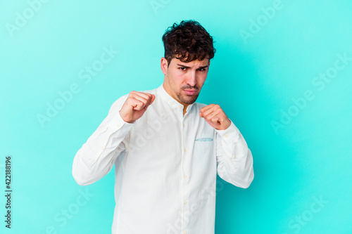 Young caucasian man isolated on blue background showing fist to camera, aggressive facial expression.