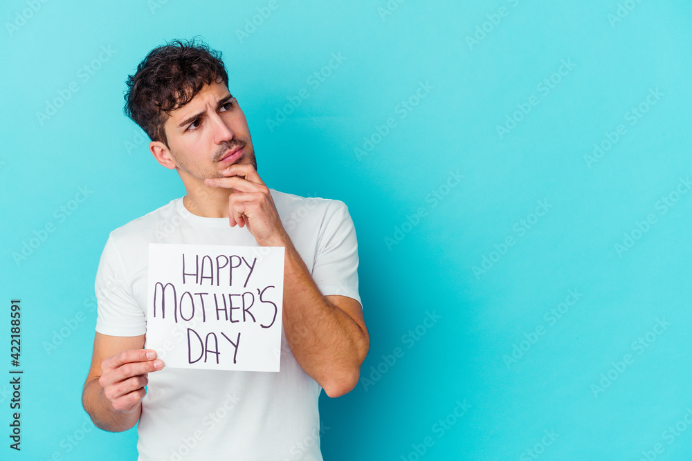 Young caucasian man holding a happy mothers day placard isolated looking sideways with doubtful and skeptical expression. Young caucasian man holding a happy mothers day placard isolated looking sideways with doubtful and skeptical expression.