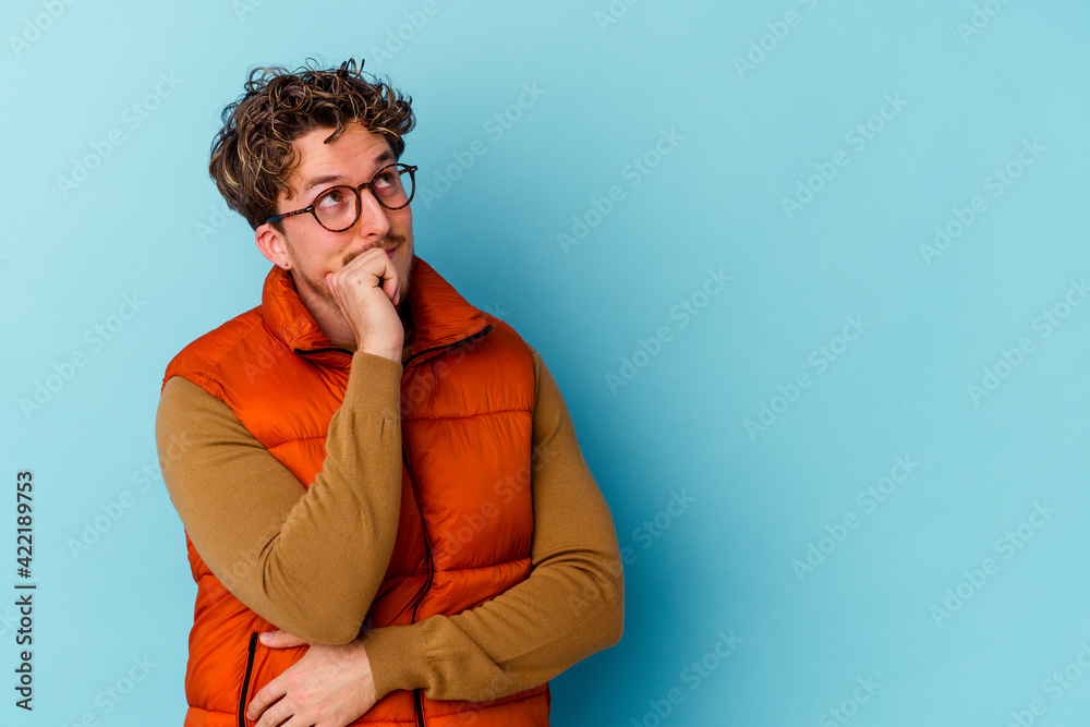 Young caucasian man wearing eyeglasses isolated on blue background relaxed thinking about something looking at a copy space. Young caucasian man wearing eyeglasses isolated on blue background relaxed thinking about something looking at a copy space.