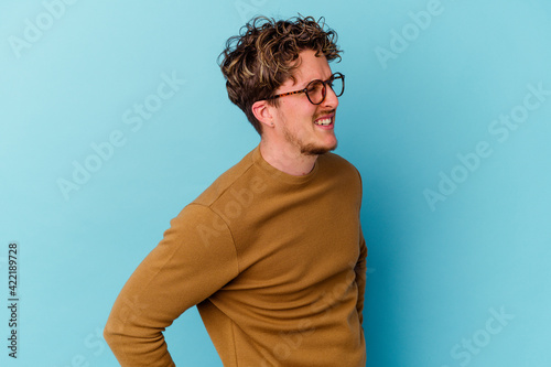 Young caucasian man wearing eyeglasses isolated on blue background suffering a back pain. © Asier