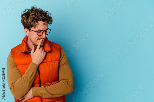 Young caucasian man wearing eyeglasses isolated on blue background looking sideways with doubtful and skeptical expression.