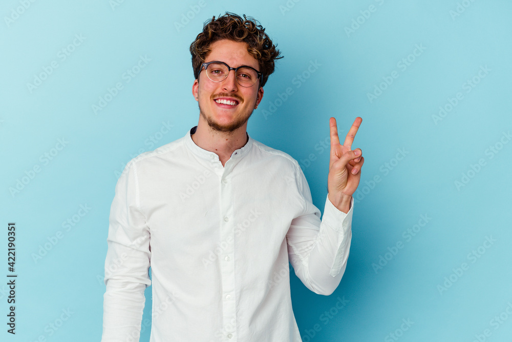 Young caucasian business man isolated on blue background joyful and carefree showing a peace symbol with fingers.
