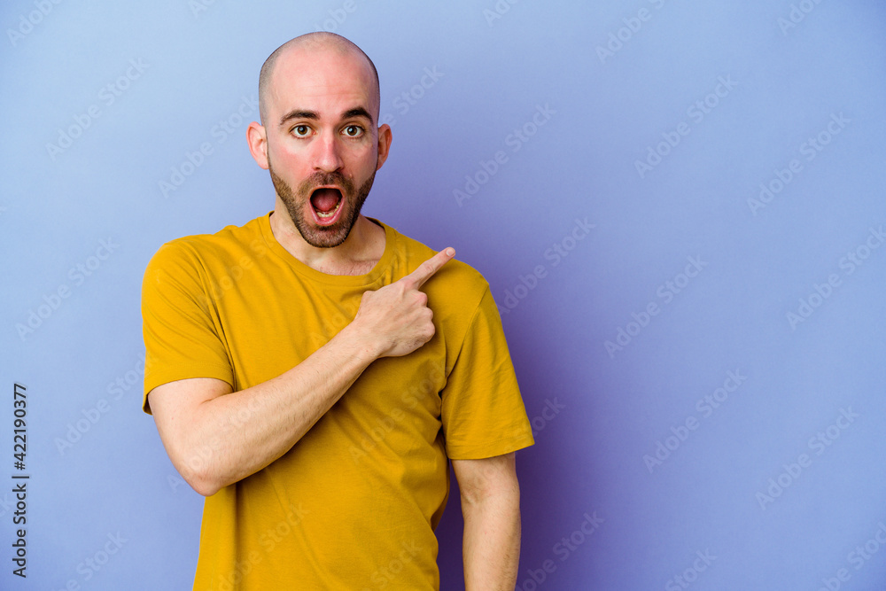 Young caucasian bald man isolated on purple background pointing to the side