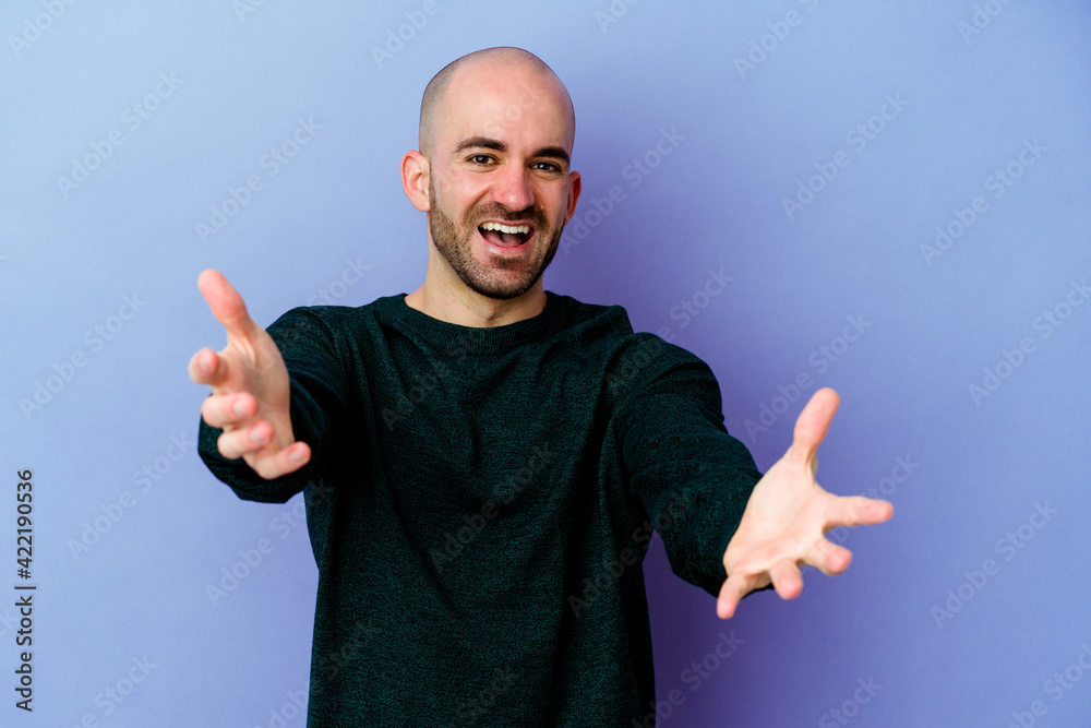 Young caucasian bald man isolated on purple background feels confident giving a hug to the camera. Young caucasian bald man isolated on purple background feels confident giving a hug to the camera.