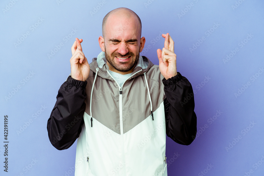 Naklejka premium Young caucasian bald man isolated on purple background crossing fingers for having luck