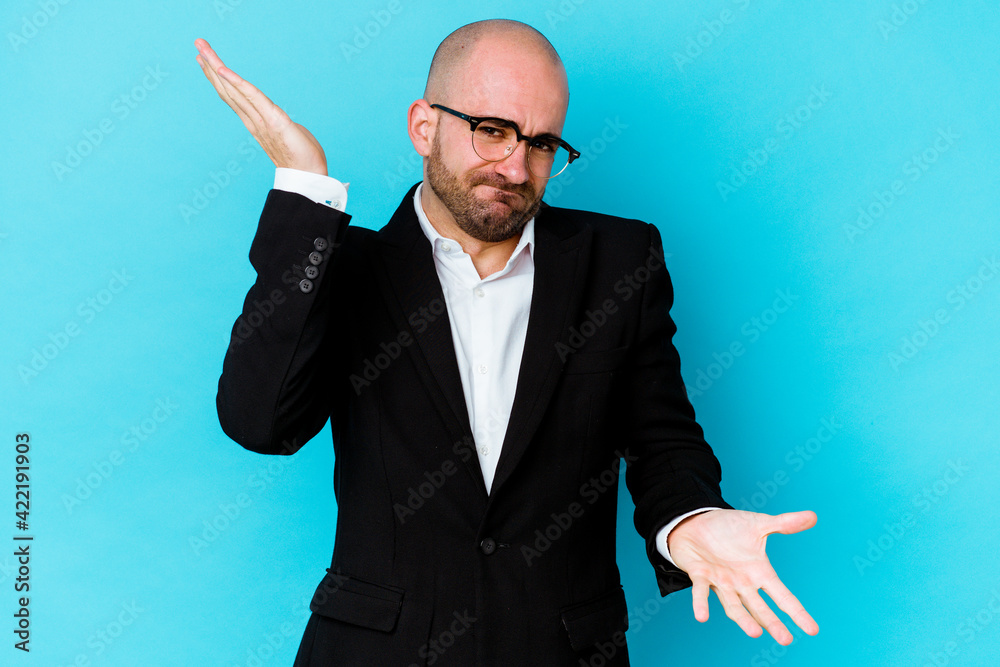 Young business caucasian bald man isolated on blue background makes scale with arms, feels happy and confident.