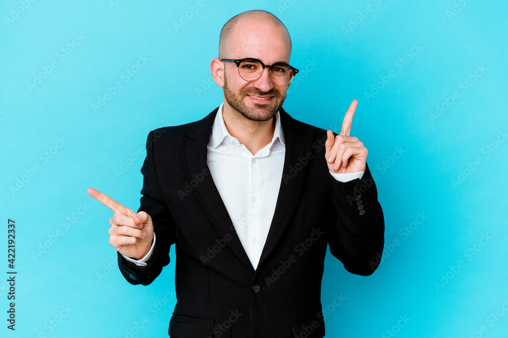 Young business caucasian bald man isolated on blue background pointing to different copy spaces, choosing one of them, showing with finger. Young business caucasian bald man isolated on blue background pointing to different copy spaces, choosing one of them, showing with finger.