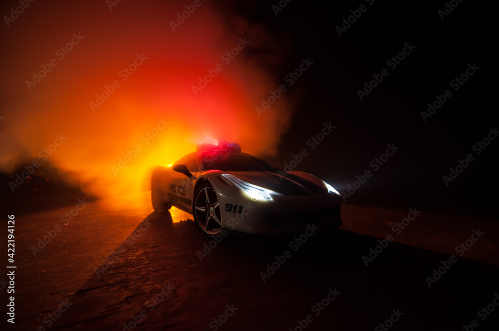Naklejka premium Police car chasing a car at night with fog background. 911 Emergency response police car speeding to scene of crime. Selective focus