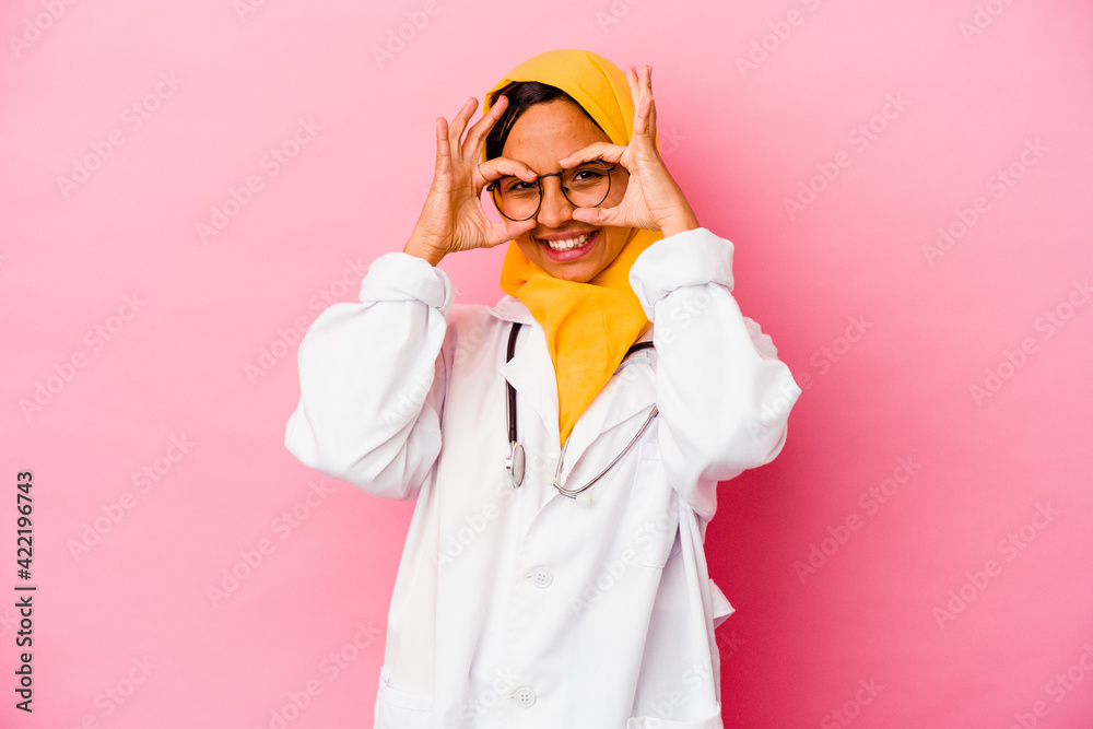 Young doctor muslim woman isolated on pink background showing okay sign over eyes Young doctor muslim woman isolated on pink background showing okay sign over eyes