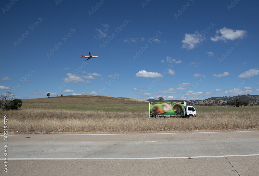 A truck and overhead plane on a freeway in an Australian Country Town midway between Sydney and Melbourne A truck and overhead plane on a freeway in an Australian Country Town midway between Sydney and Melbourne