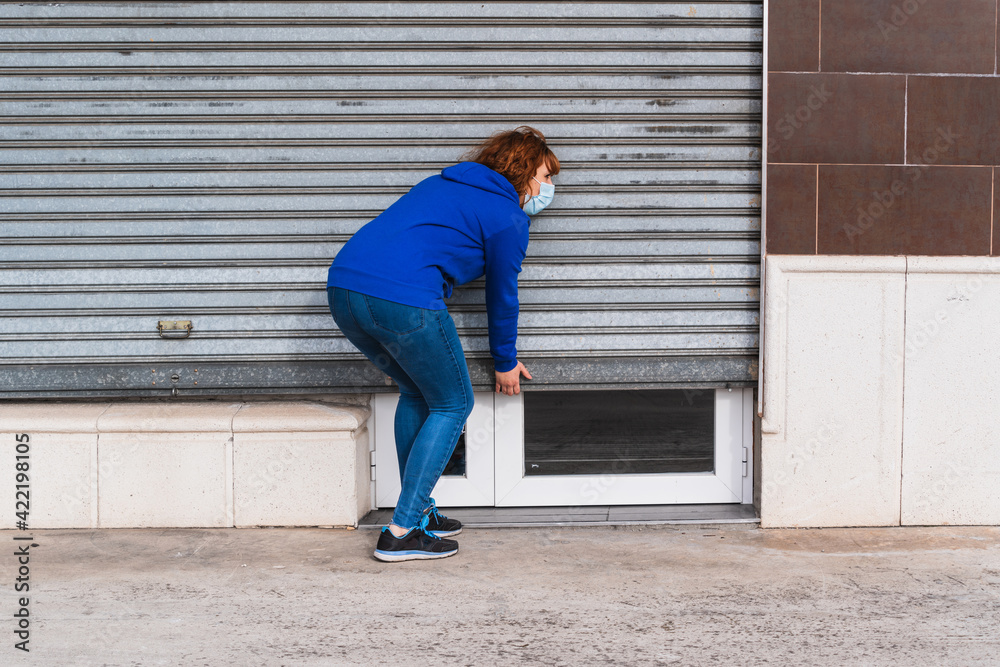 young woman with a mask opening the shutter of her business young woman with a mask opening the shutter of her business