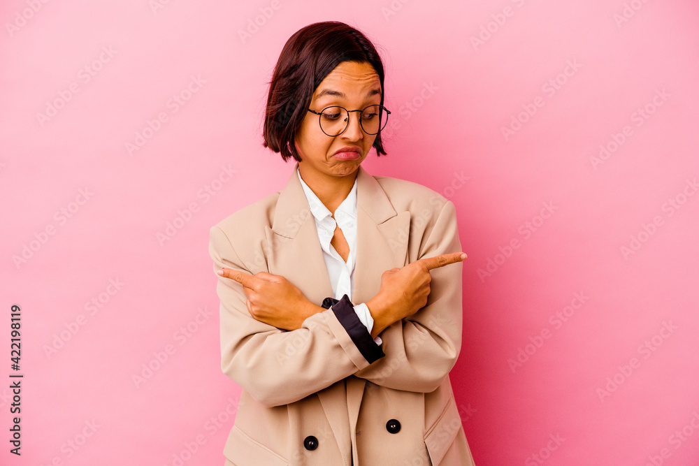 Young business mixed race woman isolated on pink background points sideways, is trying to choose between two options. Young business mixed race woman isolated on pink background points sideways, is trying to choose between two options.