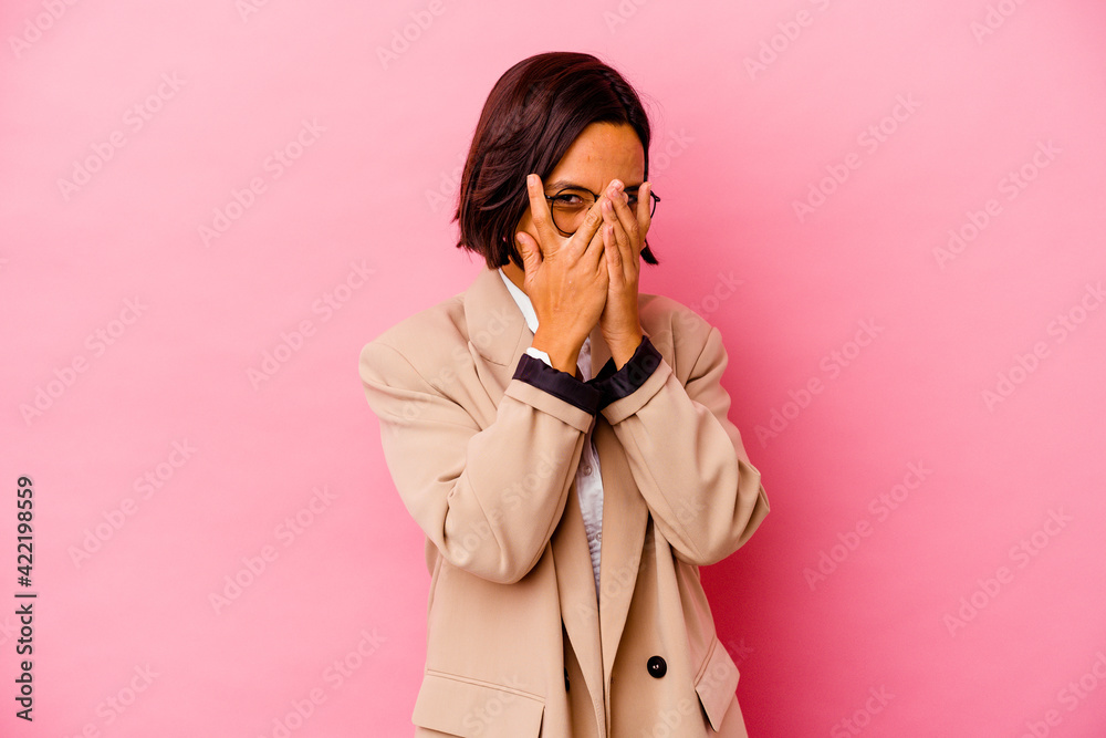 Young business mixed race woman isolated on pink background blink at the camera through fingers, embarrassed covering face.