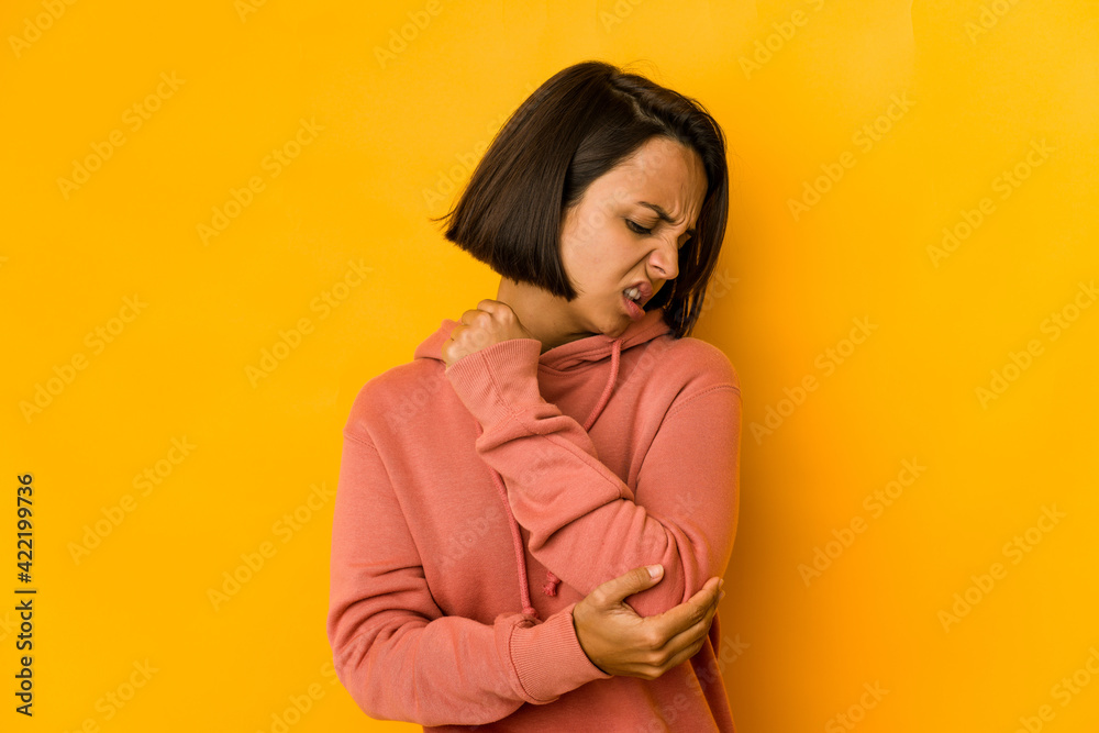 Young hispanic woman isolated on yellow massaging elbow, suffering after a bad movement. Young hispanic woman isolated on yellow massaging elbow, suffering after a bad movement.