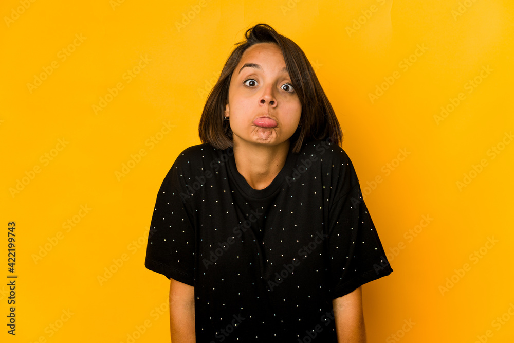 Young hispanic woman isolated on yellow shrugs shoulders and open eyes confused.