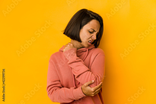 Young hispanic woman isolated on yellow massaging elbow, suffering after a bad movement. © Asier