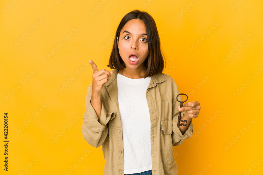 Young hispanic woman holding an old key having an idea, inspiration concept. Young hispanic woman holding an old key having an idea, inspiration concept.