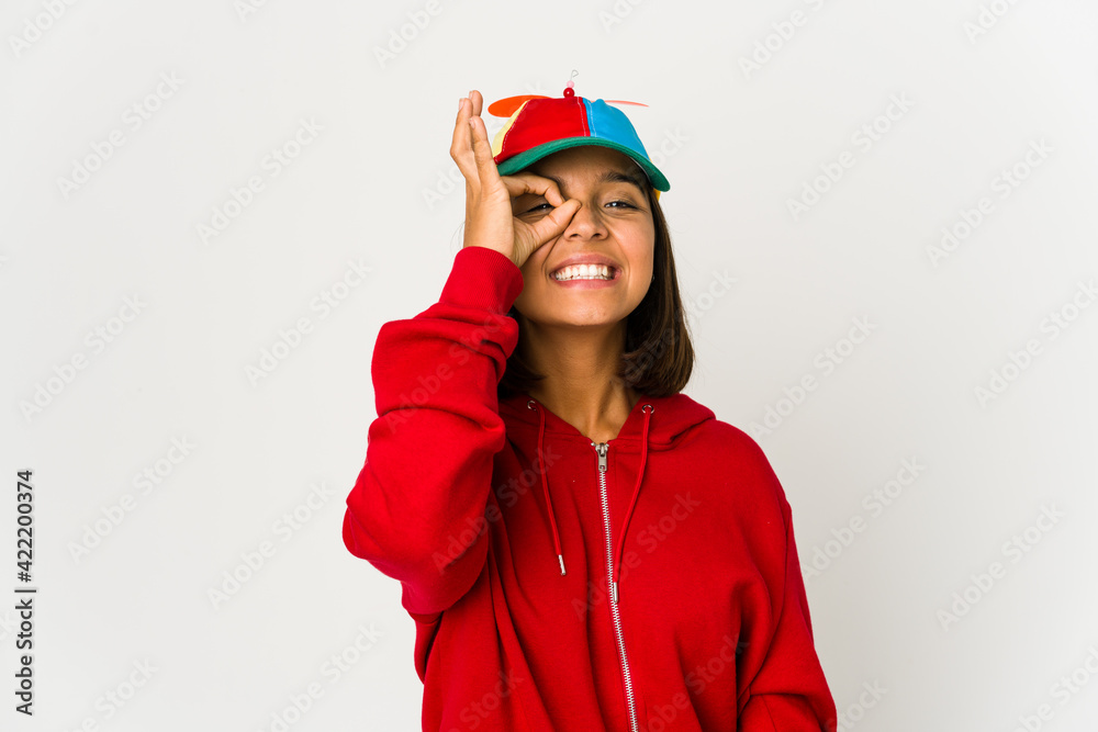 Young hispanic woman wearing a cap with propeller isolated excited keeping ok gesture on eye. Young hispanic woman wearing a cap with propeller isolated excited keeping ok gesture on eye.