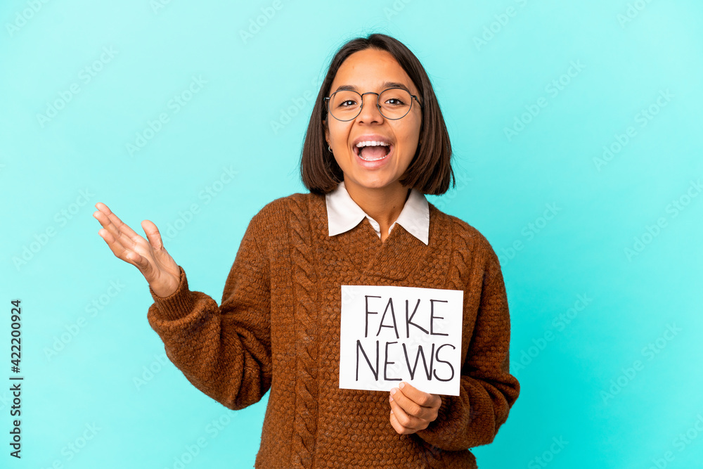 Young hispanic mixed race woman holding a fake news placard receiving a pleasant surprise, excited and raising hands. Young hispanic mixed race woman holding a fake news placard receiving a pleasant surprise, excited and raising hands.