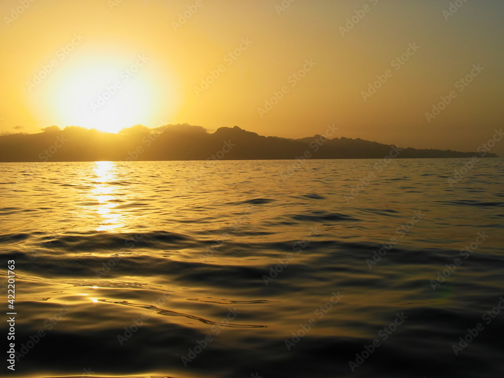The sun rises over a Caribbean island, coasts of Dominica seen from the deck of a sailing boat. The sun rises over a Caribbean island, coasts of Dominica seen from the deck of a sailing boat.