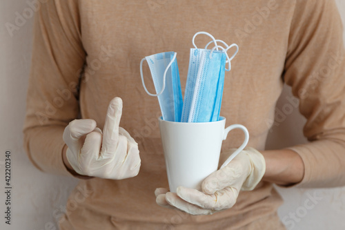Hand in white gloves holding a ceramic cup with blue masks and other hand showing middle finger