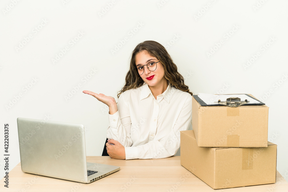 Young caucasian worker of a parcel company isolated showing a copy space on a palm and holding another hand on waist. Young caucasian worker of a parcel company isolated showing a copy space on a palm and holding another hand on waist.