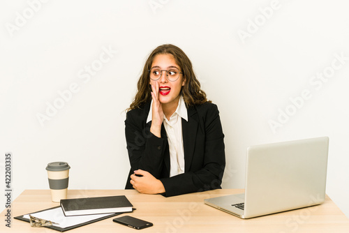 Young caucasian business woman working on her desktop isolated is saying a secret hot braking news and looking aside