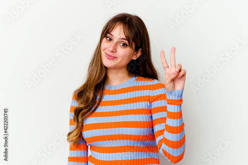 Young caucasian cute woman isolated on white background joyful and carefree showing a peace symbol with fingers.