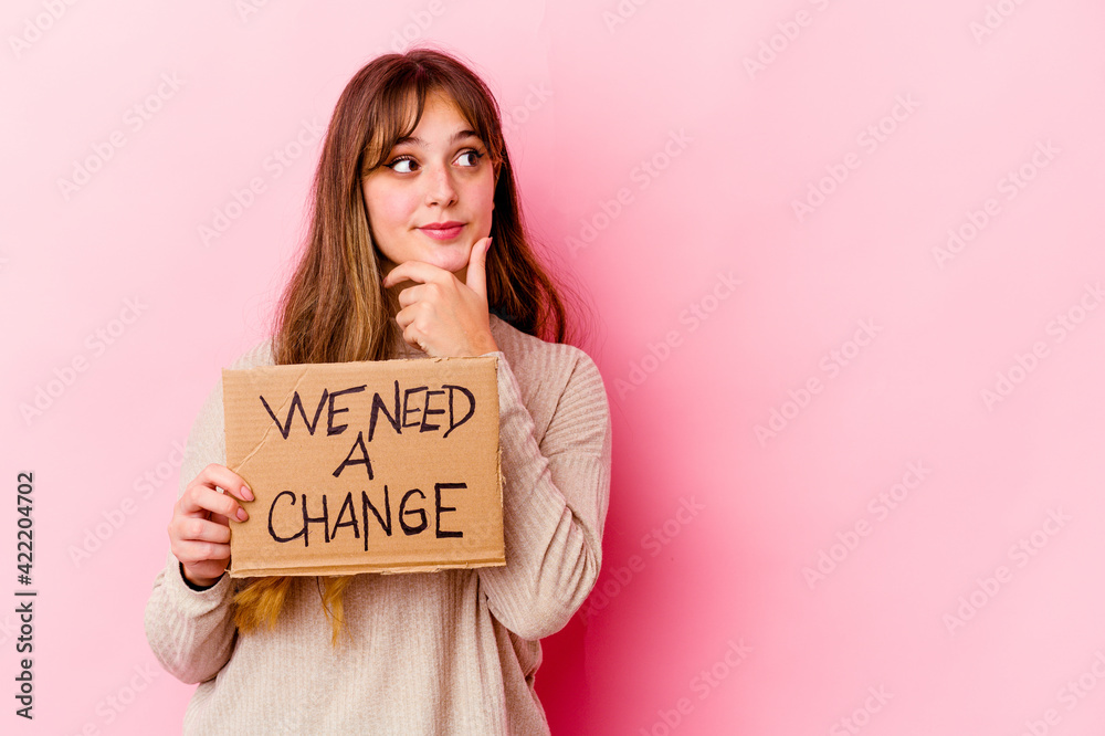 Young caucasian woman holding a We need a change placard isolated looking sideways with doubtful and skeptical expression. Young caucasian woman holding a We need a change placard isolated looking sideways with doubtful and skeptical expression.