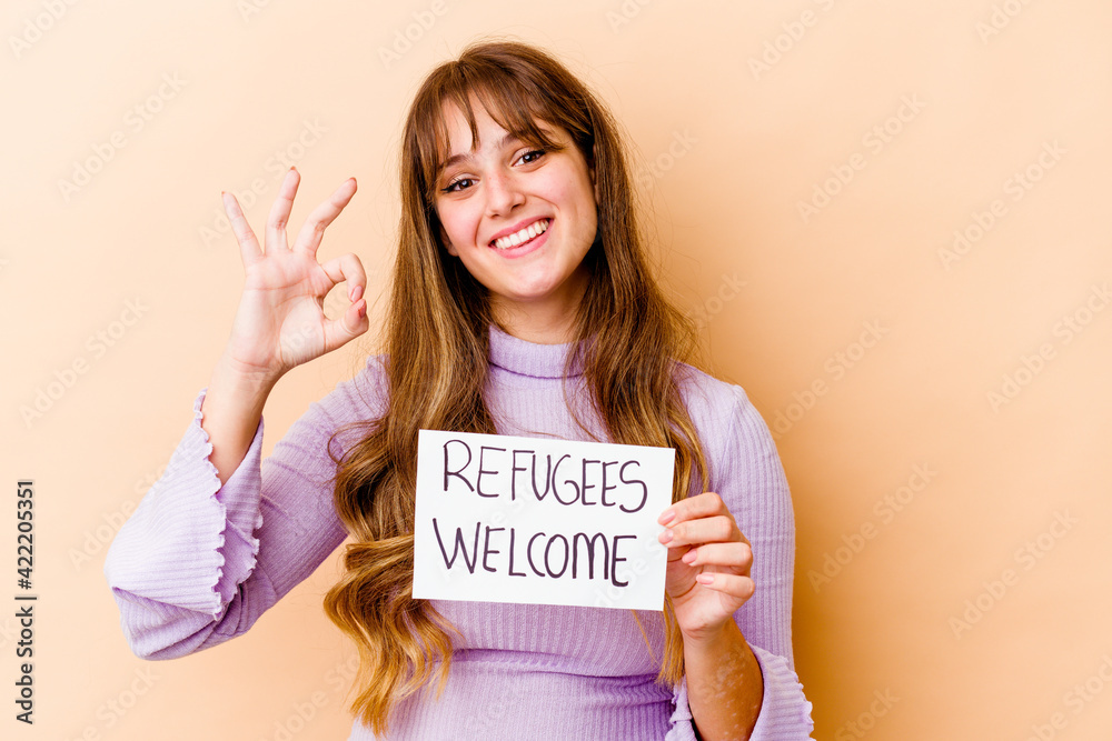 Young caucasian woman holding a Refugees welcome placard isolated cheerful and confident showing ok gesture. Young caucasian woman holding a Refugees welcome placard isolated cheerful and confident showing ok gesture.