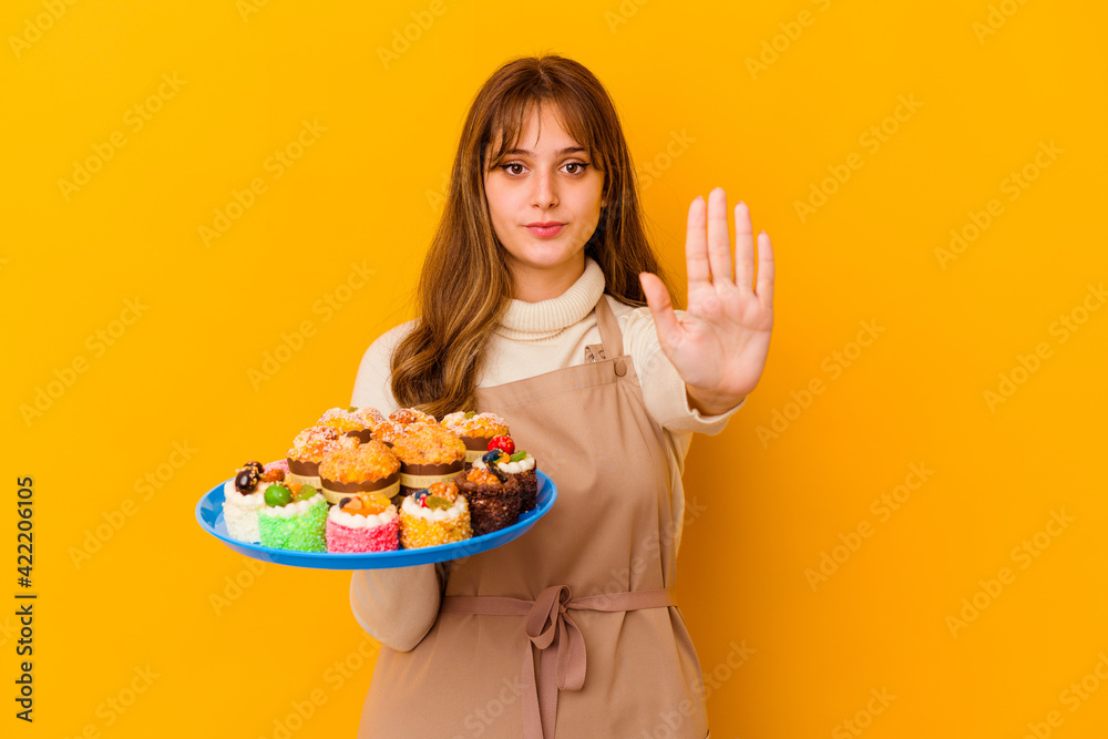 Young pastry chef woman isolated on yellow background standing with outstretched hand showing stop sign, preventing you.