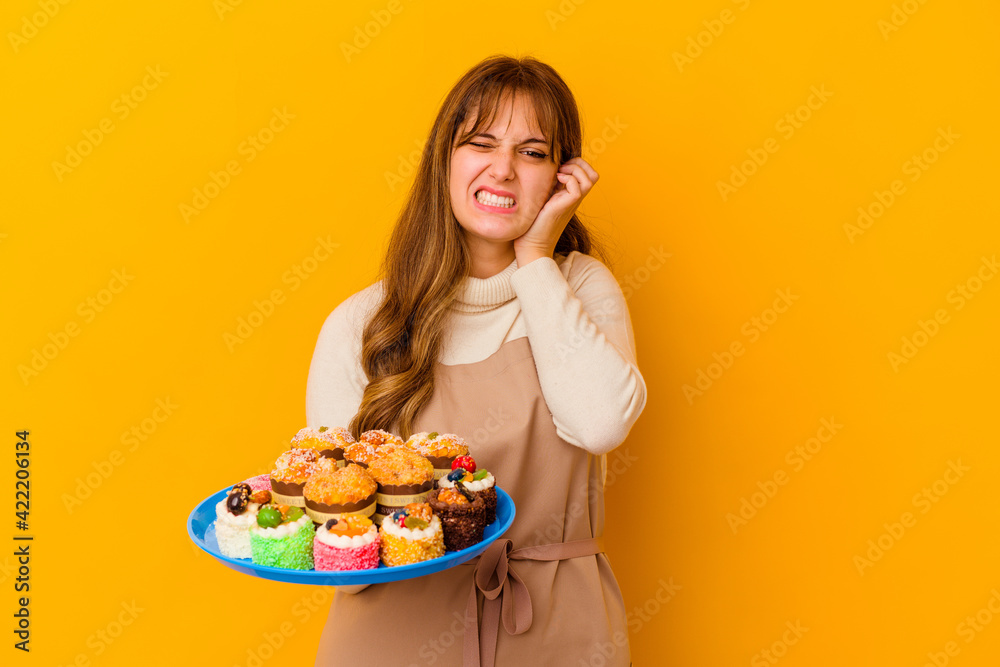 Young pastry chef woman isolated on yellow background covering ears with hands.