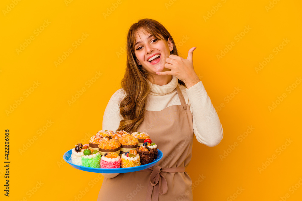 Young pastry chef woman isolated on yellow background showing a mobile phone call gesture with fingers.