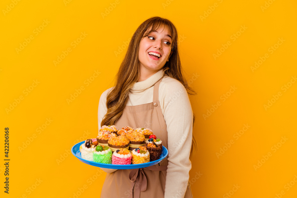 Young pastry chef woman isolated on yellow background looks aside smiling, cheerful and pleasant.