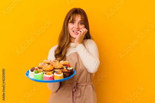 Young pastry chef woman isolated on yellow background biting fingernails  nervous and very anxious.