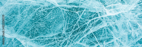 Texture of beautiful blue ice with cracks and air bubbles in the frozen lake. Winter nature background. Lake Baikal, Siberia, Russia. Banner.