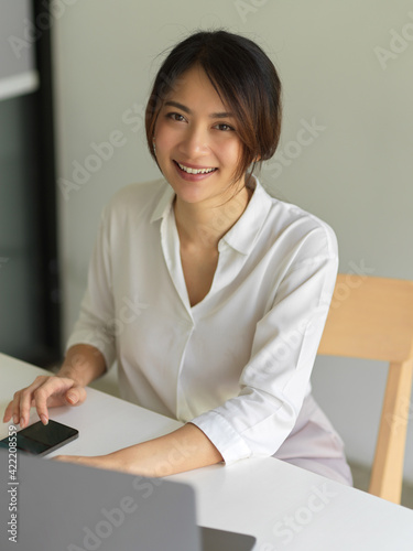 Work from home concept, female worker smiling to camera while sitting at workspace in living room