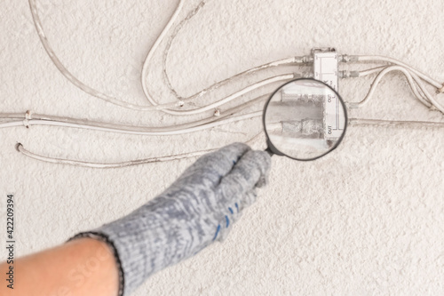 The hand of an industrial worker in a construction glove examines a large antenna splitter with a magnifying glass