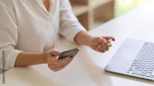 Female online shopping on smartphone and holding debit card in her hand to online payment