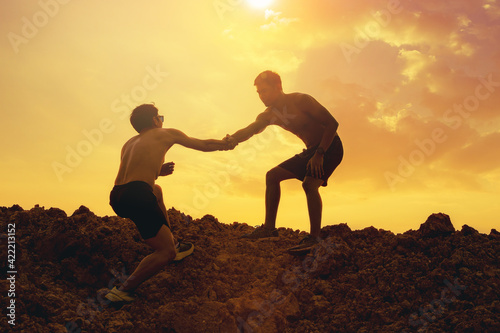 Trail runner with hand helping each other hike up a mountain top together with sunset background. Help and support concept. 