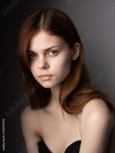 Portrait of a beautiful woman with bare shoulders red hair close-up gray background cropped view